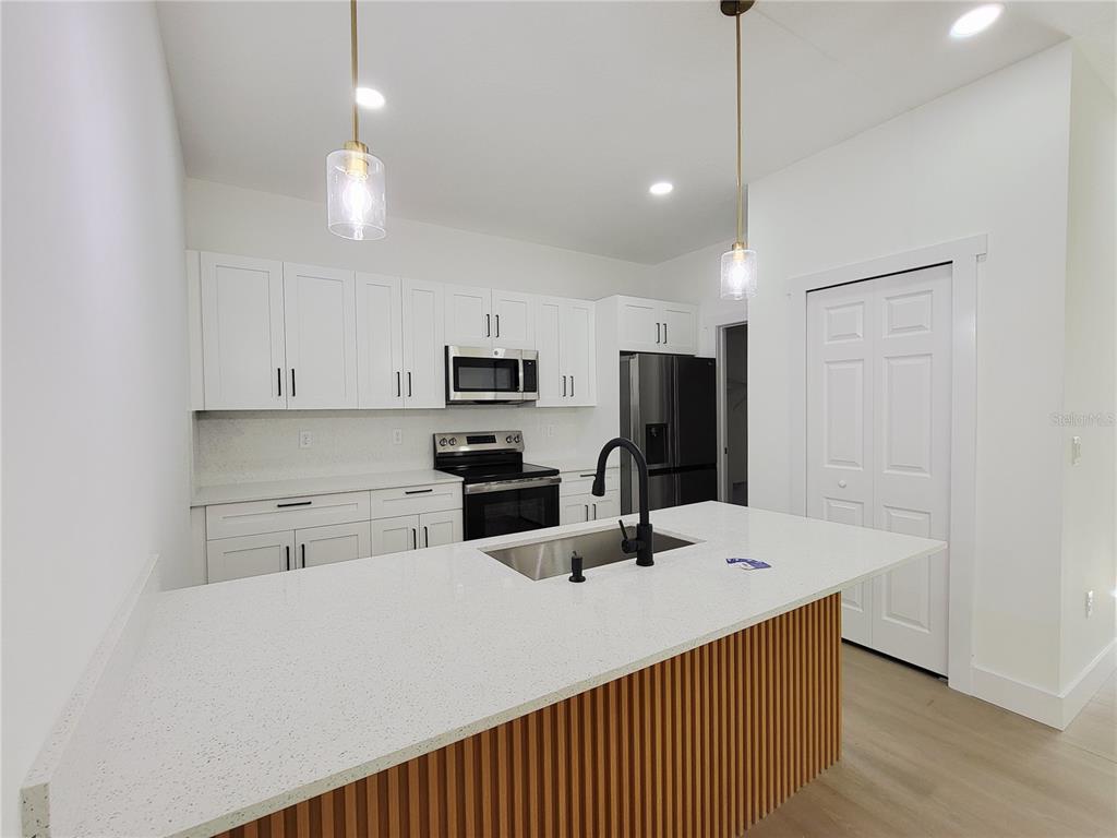A modern kitchen features white cabinets, stainless steel appliances, and a slatted wood kitchen island — 1751 NANDINA COURT NW, PALM BAY, FL