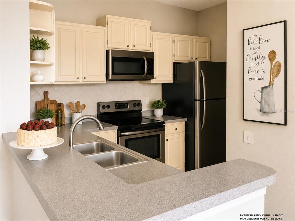 A kitchen features cream cabinets, a black microwave and refrigerator, and a gray countertop — 1420 LAKE SHADOW CIRCLE UNIT 9306, MAITLAND, FL