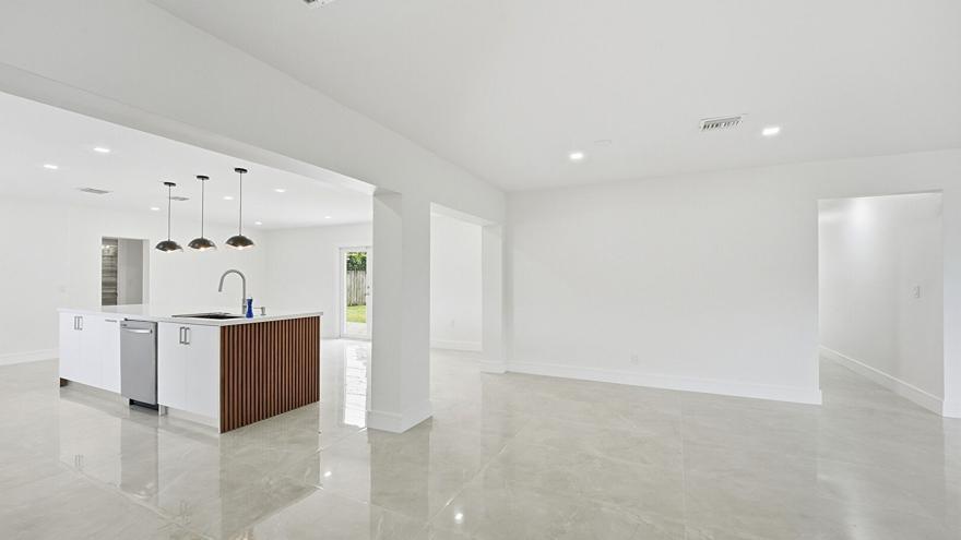 A modern kitchen with a slatted wood island and white cabinets opens to a living area — 21020 Highland Lakes Boulevard, Miami FL 33179, MIAMI, FL