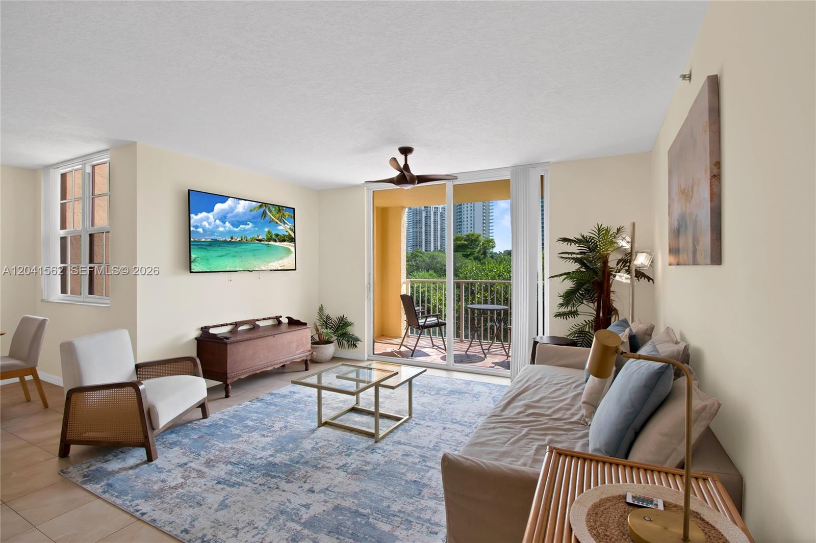 A living room features a television, a glass coffee table, and a balcony with views — AVENTURA, FL