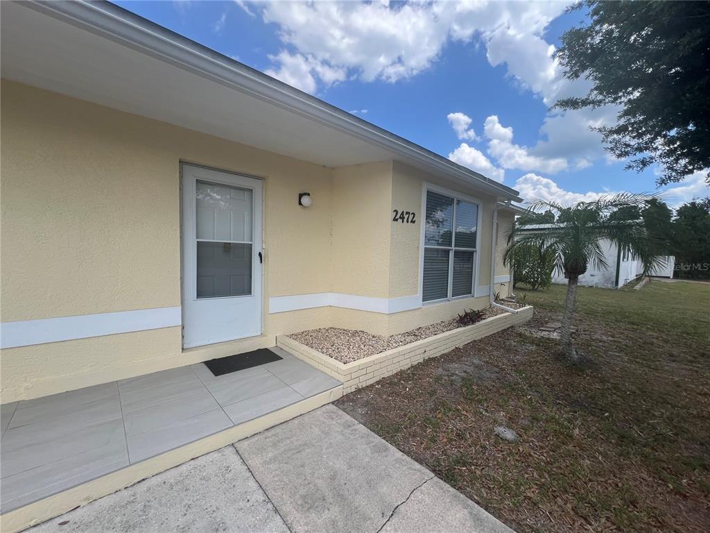 A light yellow house exterior features a front door, a window, and a tiled porch — 2472 PICNIC STREET, PORT CHARLOTTE, FL