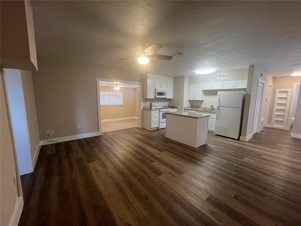 An open-concept kitchen and living area feature wood-look flooring, white cabinetry, and a center island — 2472 PICNIC STREET, PORT CHARLOTTE, FL