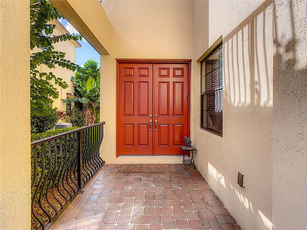 A covered entryway features a brick-paved floor, a double red door, and a metal railing — 10767 WILLOW RIDGE LOOP, ORLANDO, FL