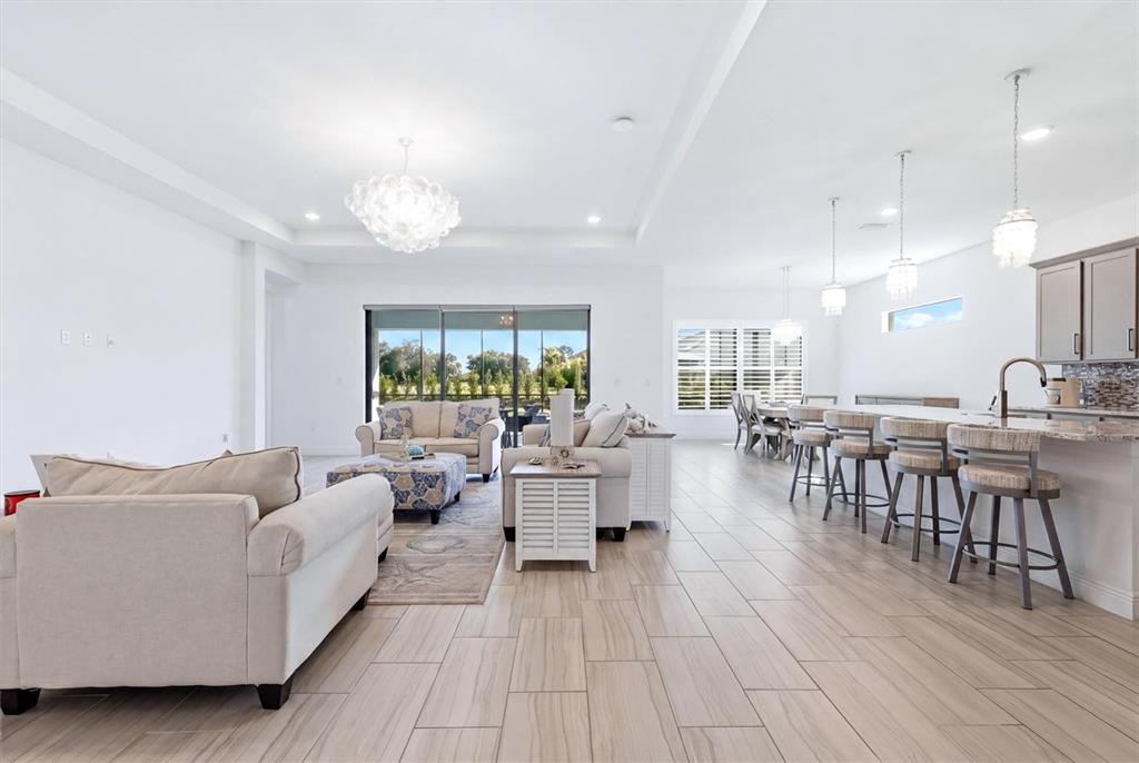 This open-concept living and dining area features tile flooring, neutral furniture, and a kitchen island — 4950 KIVA CIRCLE, BRADENTON, FL