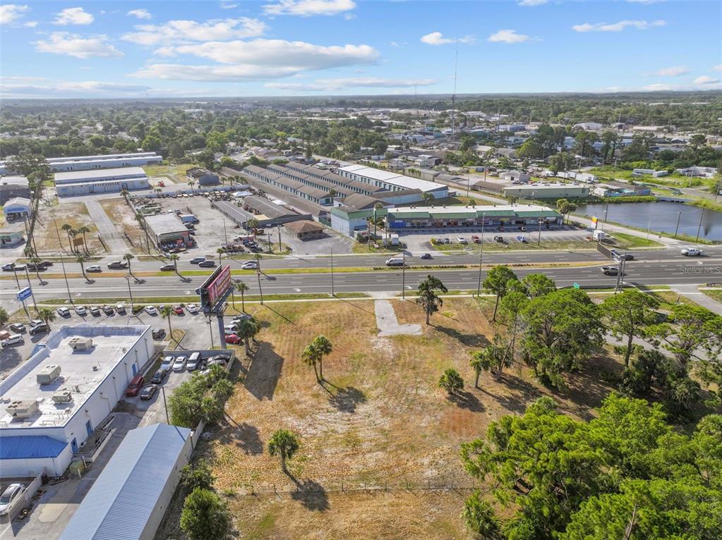 An aerial view shows a vacant grassy lot situated next to a commercial building and road — 8807 S US 19 HIGHWAY W, PORT RICHEY, FL