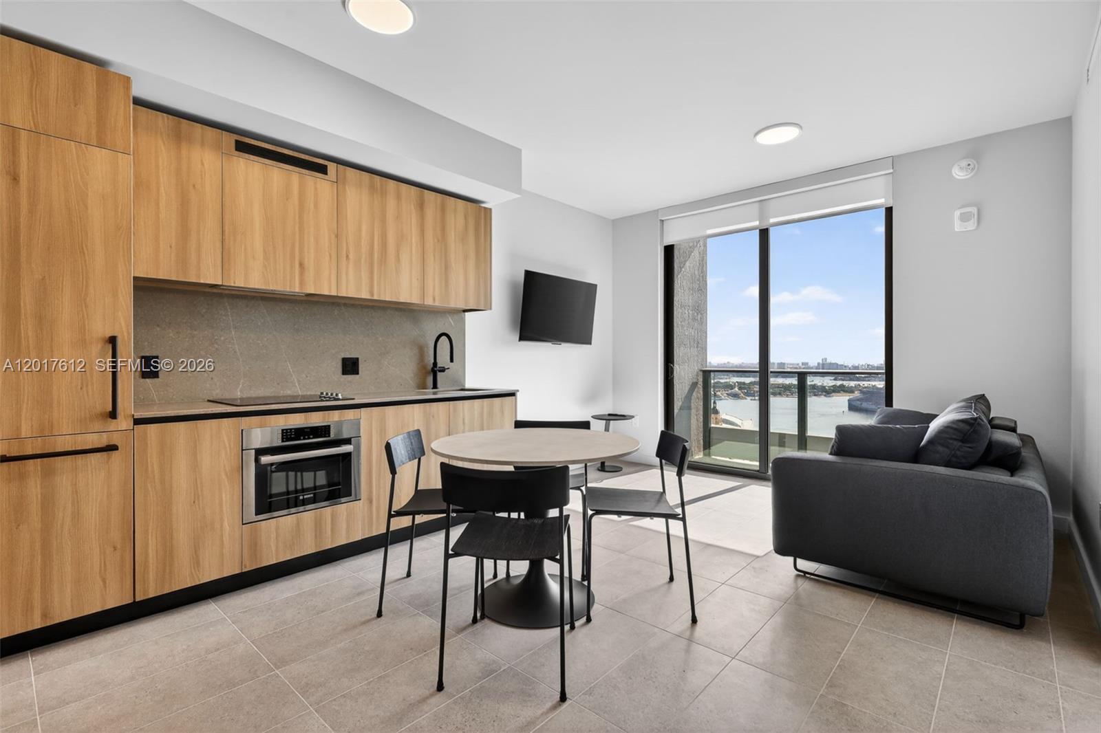 A modern studio apartment features a kitchen with wood cabinetry, a dining set, and balcony views — 121 NE 5th St # 3313, Miami FL 33132, MIAMI, FL