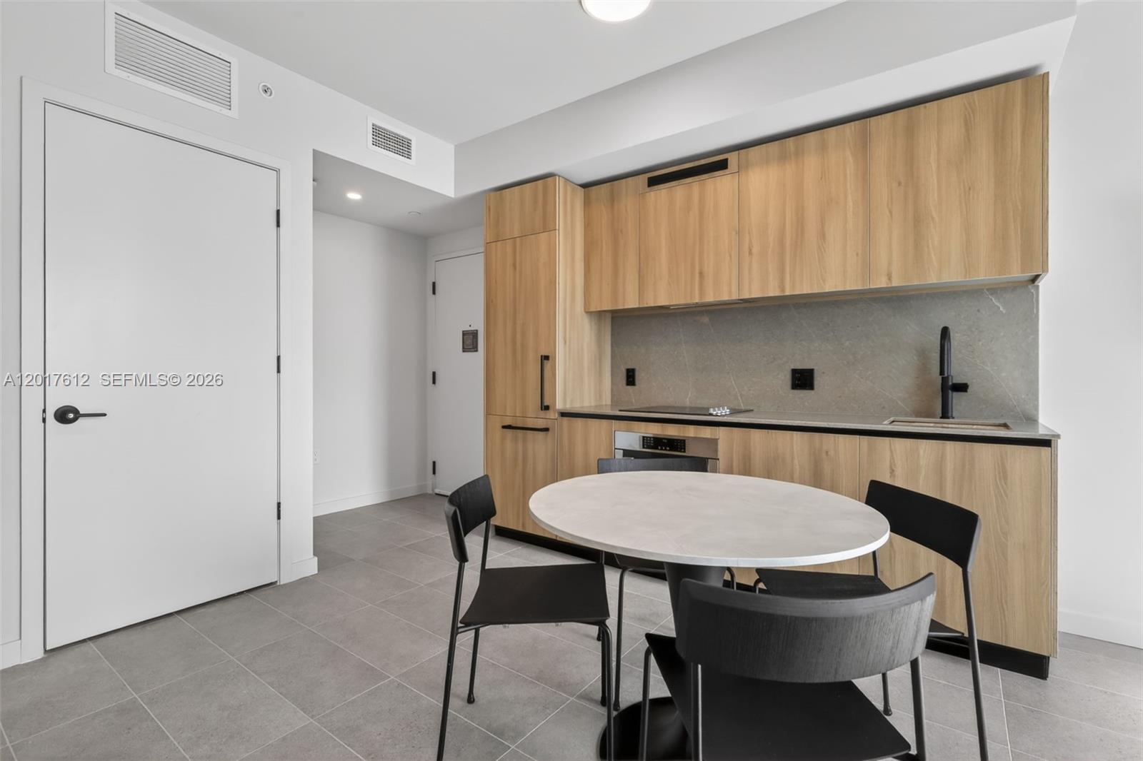 A modern kitchen features light wood cabinetry, a stone backsplash, and a small dining table — 121 NE 5th St # 3313, Miami FL 33132, MIAMI, FL