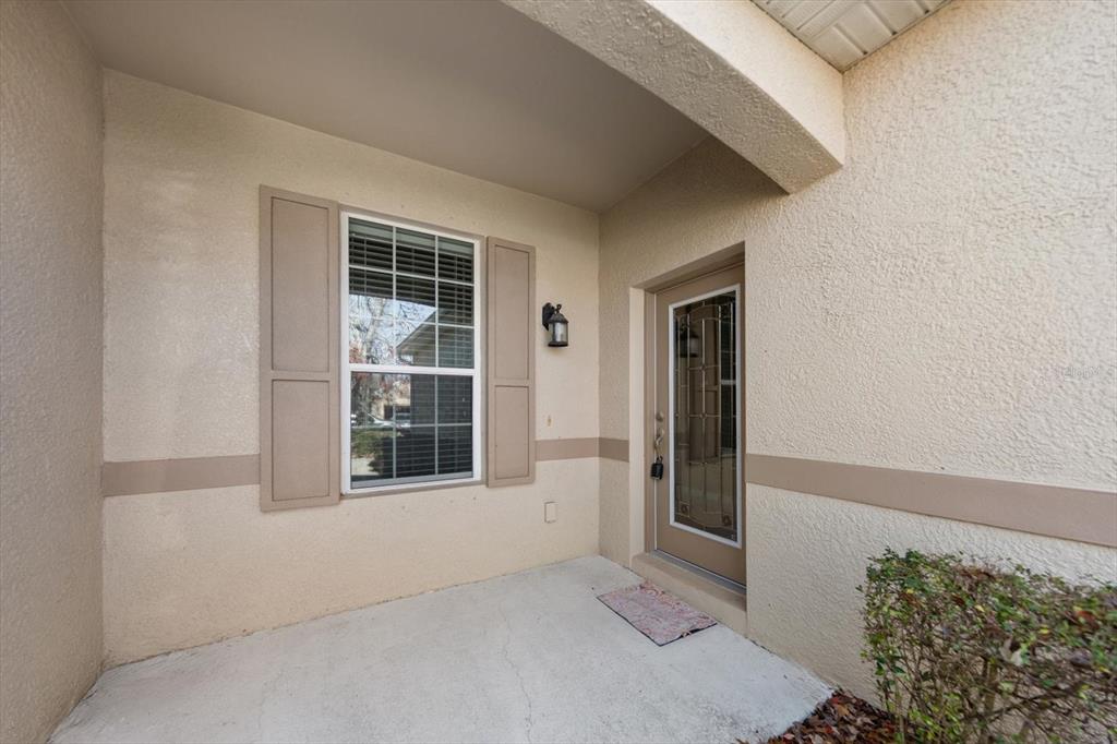 A covered entryway features a beige stucco exterior, a single window with shutters, and a door — 2302 BARRACUDA COURT, HOLIDAY, FL