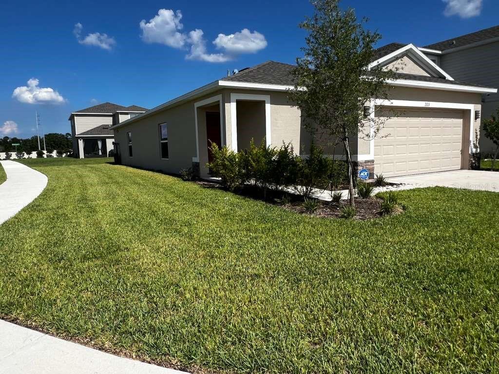 A tan single-story house with a two-car garage and a landscaped front yard — 205 ACORN ROAD, HAINES CITY, FL