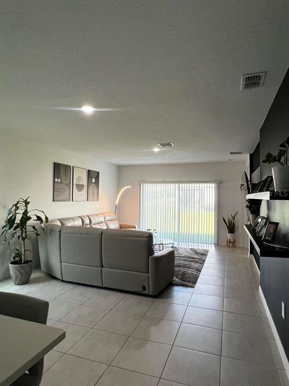 A living room features a large gray sectional sofa, tile flooring, and a sliding glass door — 205 ACORN ROAD, HAINES CITY, FL
