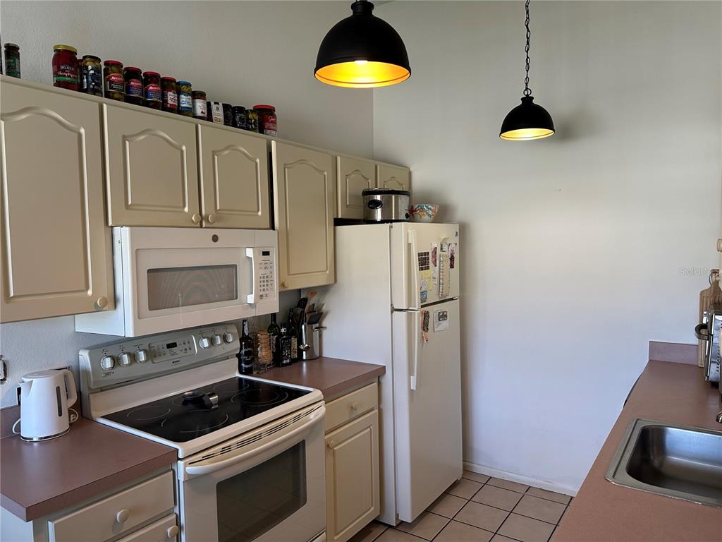 A kitchen features beige cabinets, a white stove and refrigerator, and two black pendant lights — 3401 36TH STREET W UNIT 3401, BRADENTON, FL