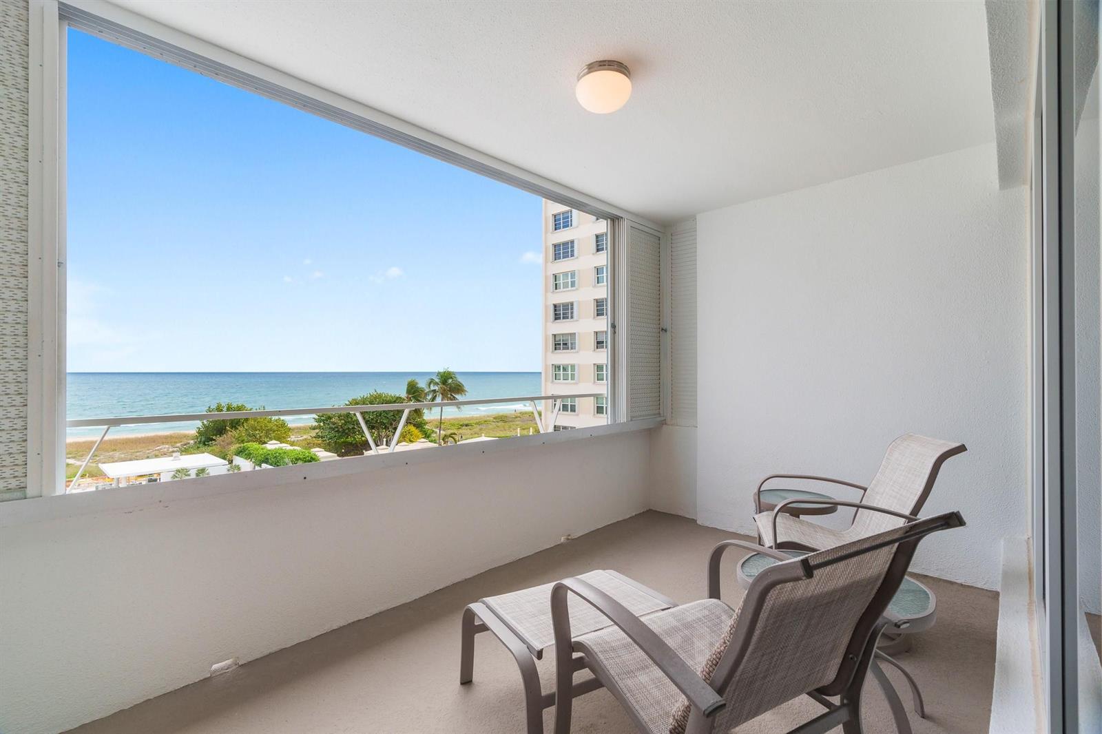 A balcony with two chairs overlooks the ocean and a neighboring building — 1850 S Ocean Boulevard # 502, Pompano Beach FL 33062, POMPANO BEACH, FL