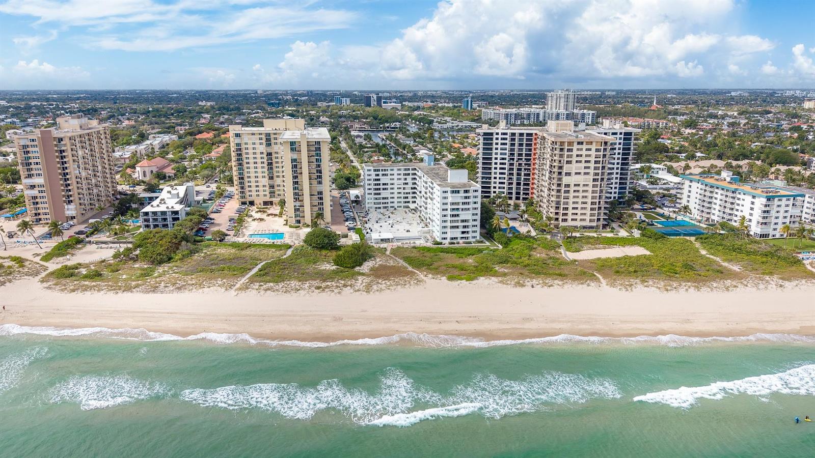An aerial view shows several high-rise apartment buildings situated along a sandy beach — 1850 S Ocean Boulevard # 502, Pompano Beach FL 33062, POMPANO BEACH, FL