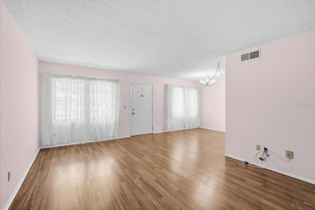 An empty living room features light pink walls, wood-look flooring, and two windows with curtains — 4910 BAY STREET NE UNIT 105, ST PETERSBURG, FL