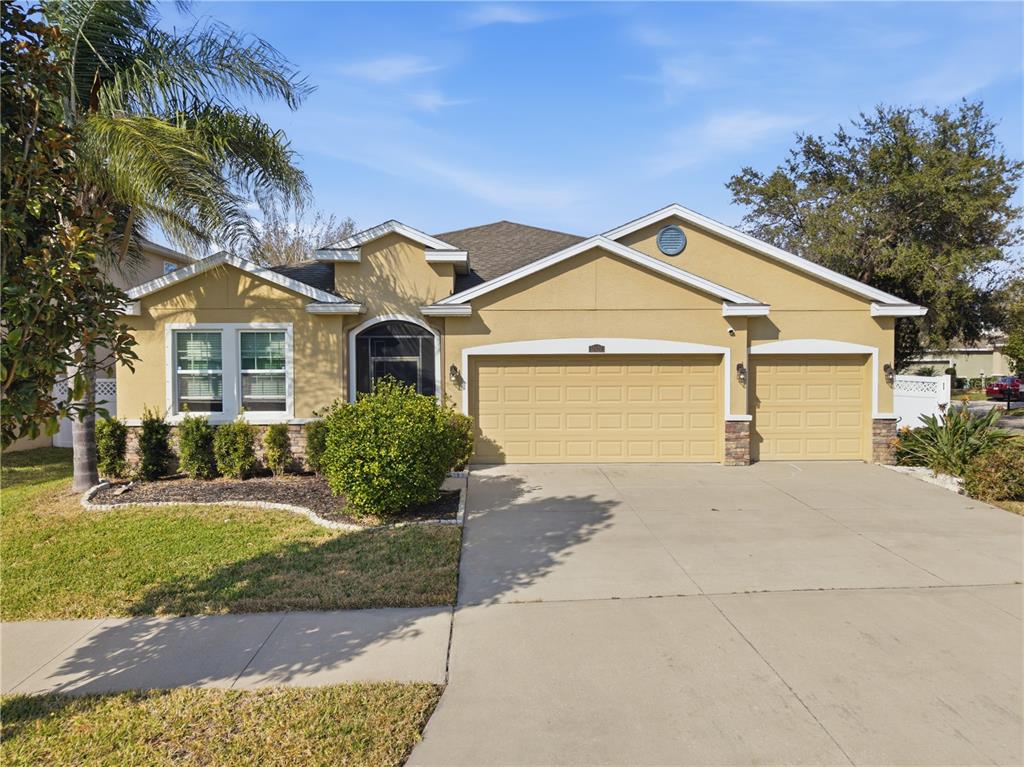 A single-story house with a tan stucco exterior, a three-car garage, and a palm tree — 10420 PLEASANT SPRING WAY, RIVERVIEW, FL