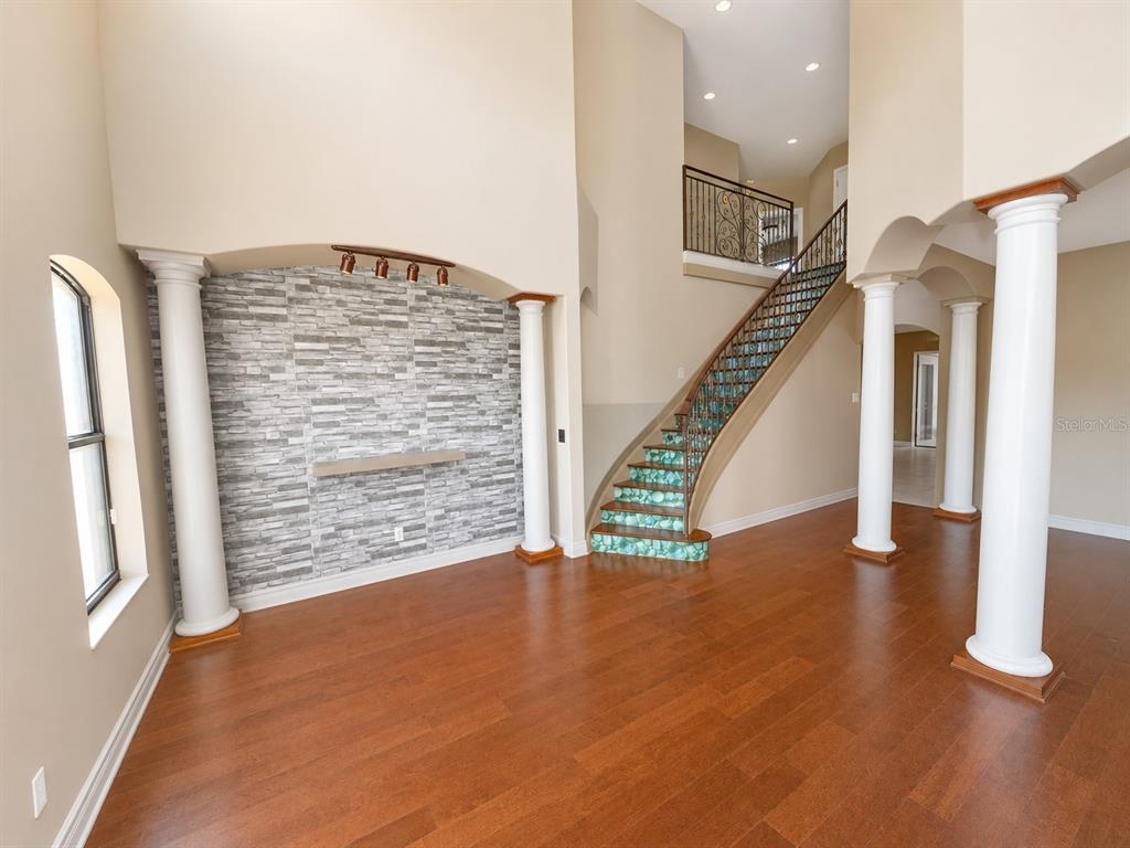 A living room features hardwood floors, a stone accent wall, and a curved staircase — 2807 VIA LARGO COURT, KISSIMMEE, FL