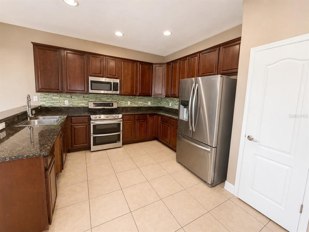 A kitchen features dark wood cabinets, stainless steel appliances, granite countertops, and a tiled floor — 2807 VIA LARGO COURT, KISSIMMEE, FL