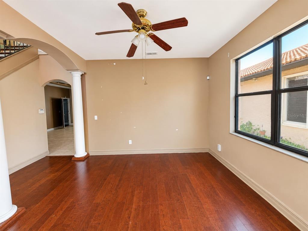 An empty room features hardwood floors, a ceiling fan, and an arched entryway with columns — 2807 VIA LARGO COURT, KISSIMMEE, FL