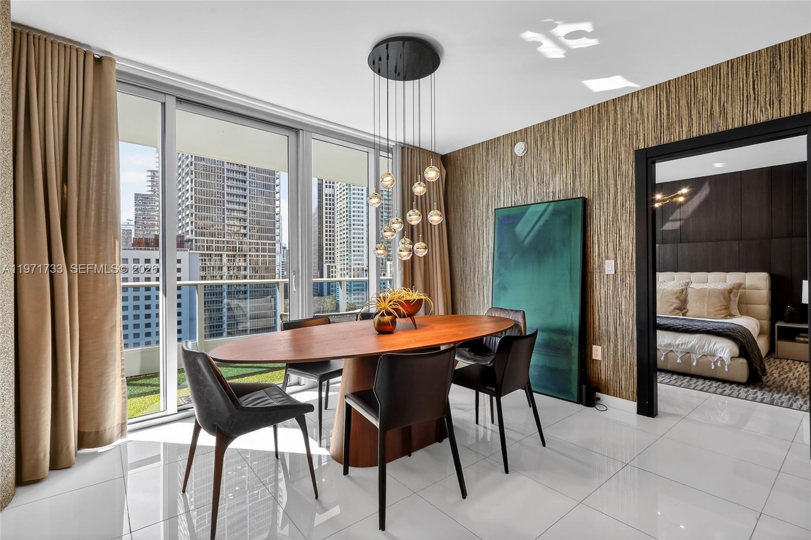 A dining room features an oval wooden table, modern pendant lights, and floor-to-ceiling windows — 200 Biscayne Boulevard Way # 1108, Miami FL 33131, MIAMI, FL