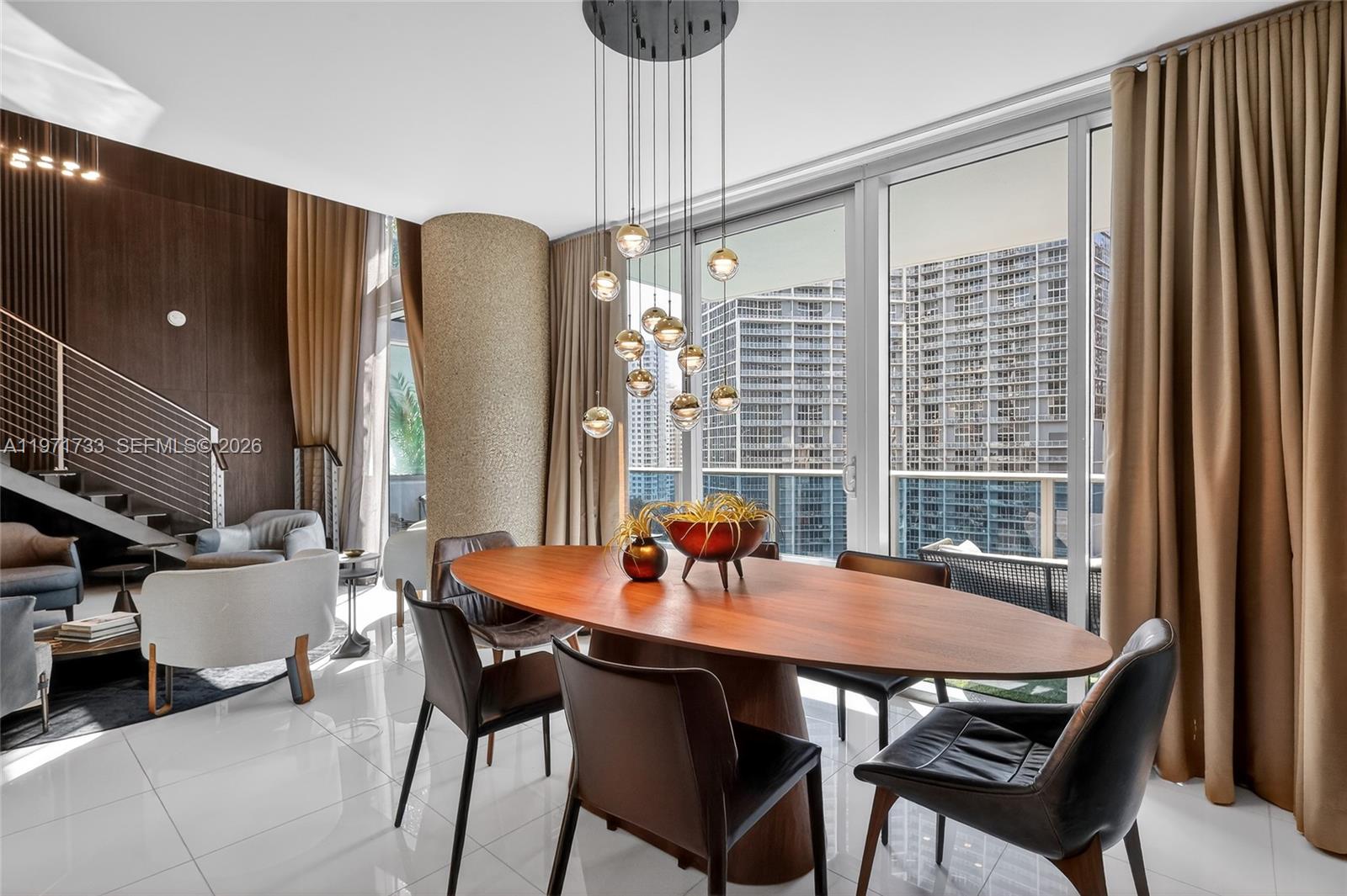 A dining area features an oval wooden table, modern pendant lights, and floor-to-ceiling windows — 200 Biscayne Boulevard Way # 1108, Miami FL 33131, MIAMI, FL