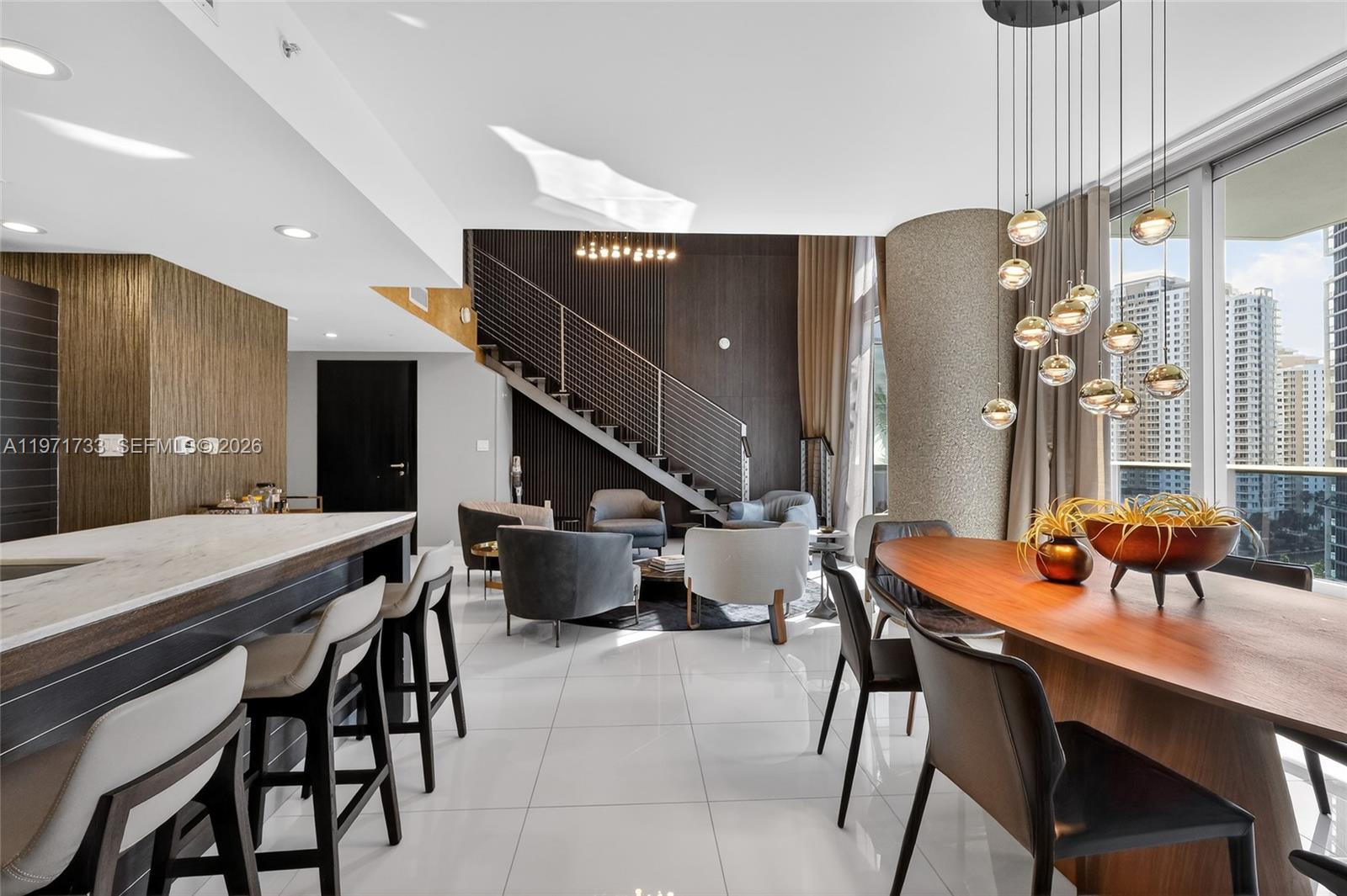 A modern open-plan living and dining area features a staircase, marble island, and city views — 200 Biscayne Boulevard Way # 1108, Miami FL 33131, MIAMI, FL