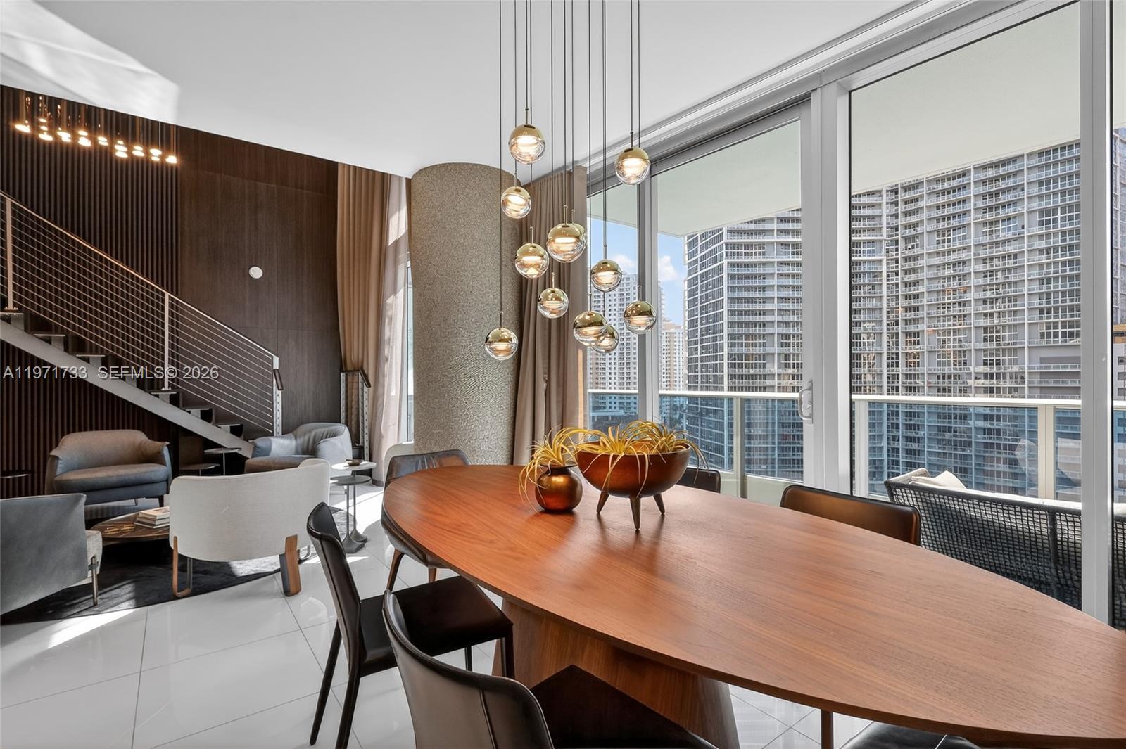 A modern dining area features a wooden oval table, pendant lights, and floor-to-ceiling windows — 200 Biscayne Boulevard Way # 1108, Miami FL 33131, MIAMI, FL
