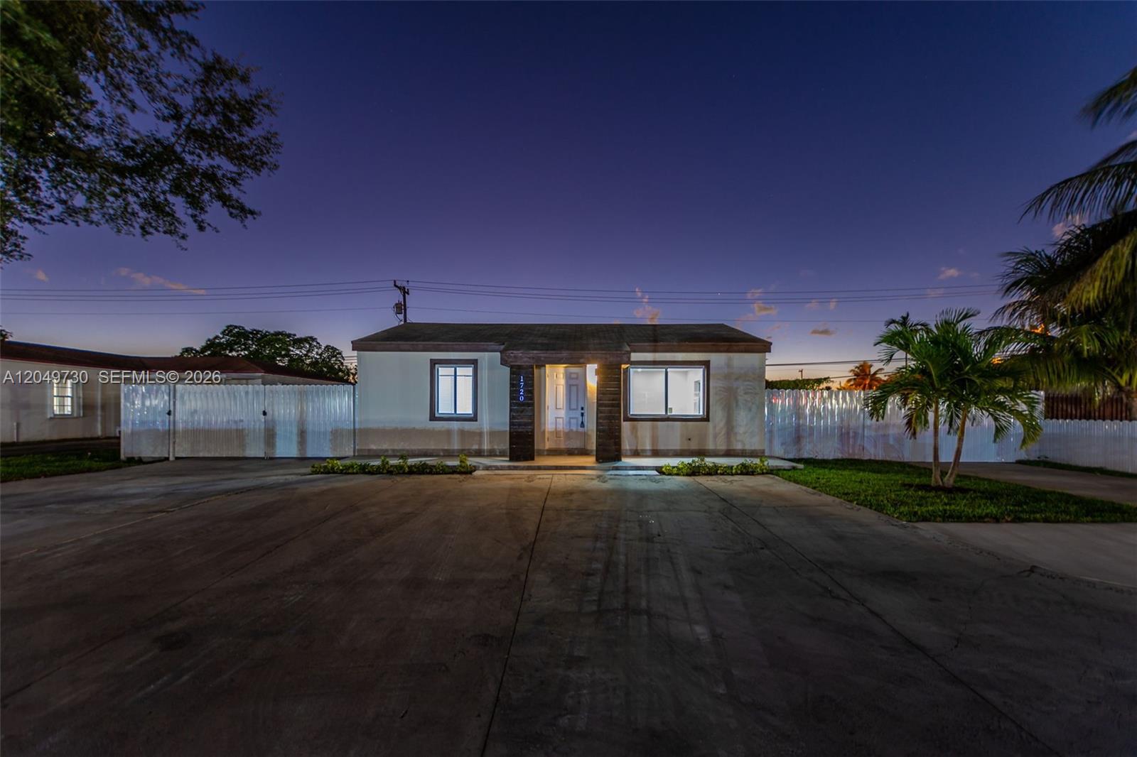 A single-story house with a concrete driveway and white fencing at dusk — 1720 NW 67th St, Miami FL 33147, MIAMI, FL