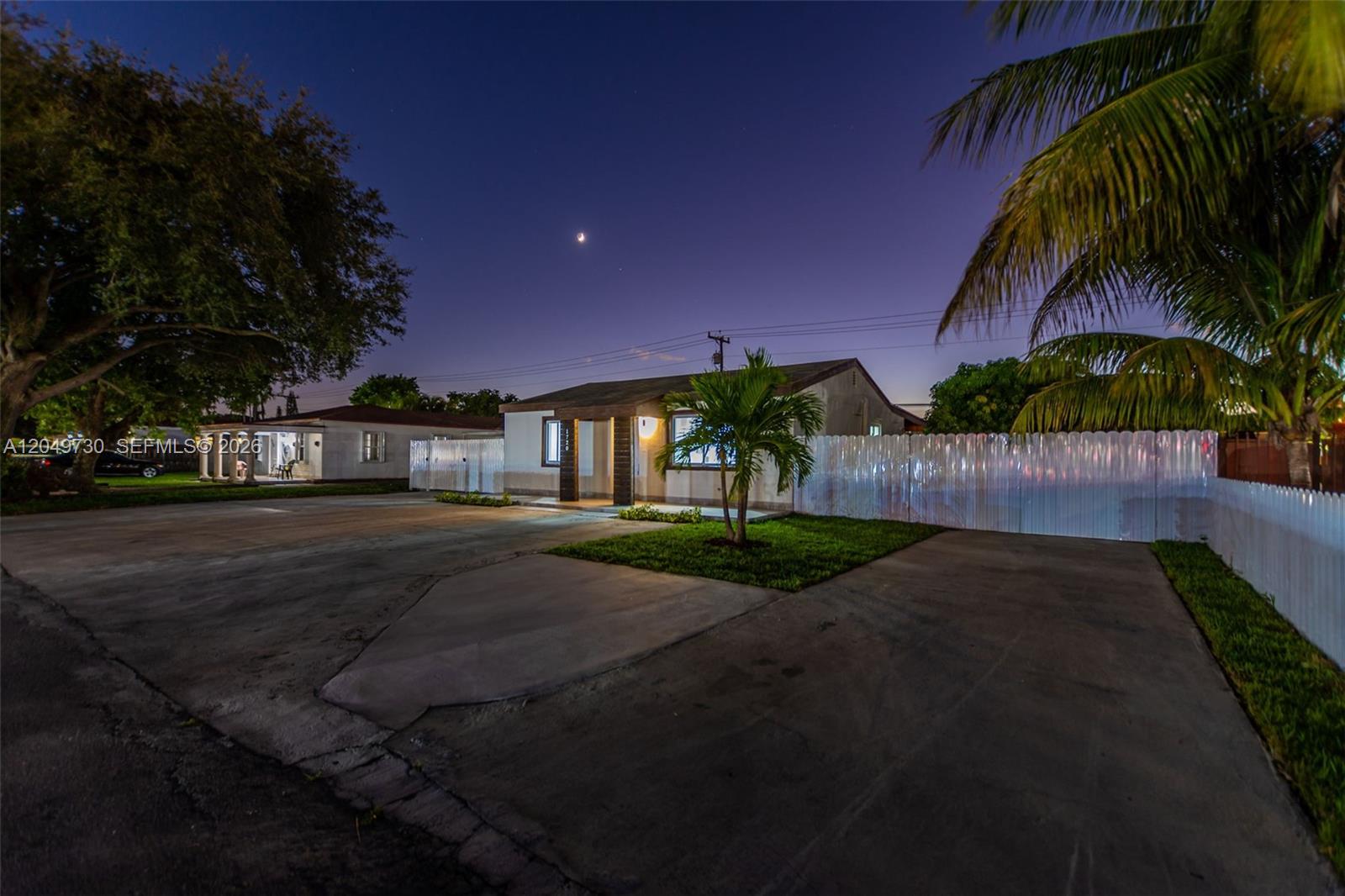 A single-story house with a concrete driveway and a white fence at twilight — 1720 NW 67th St, Miami FL 33147, MIAMI, FL