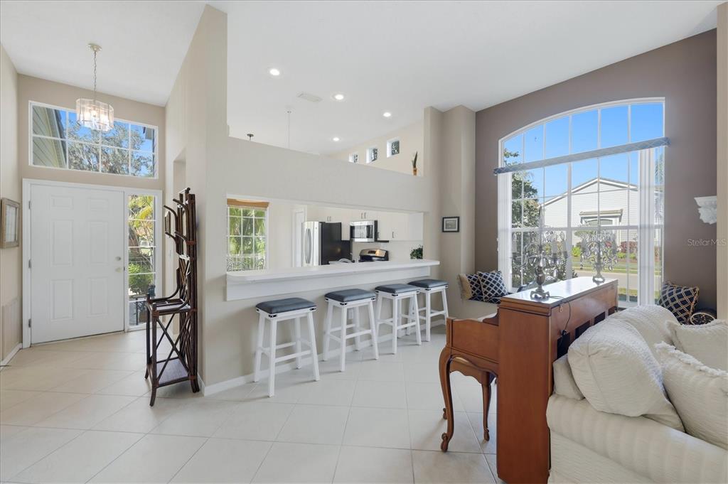A living room with a breakfast bar, piano, and large windows overlooking a suburban street — 7630 WHITEBRIDGE GLEN, UNIVERSITY PARK, FL