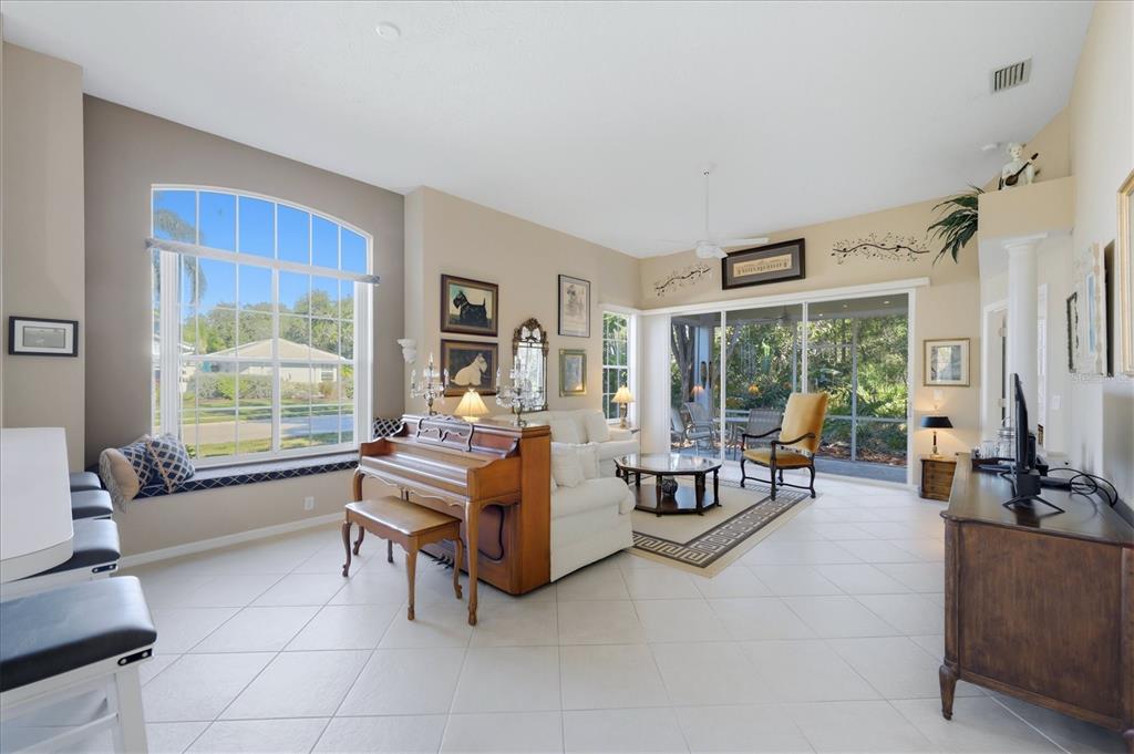 A living room features a piano, white sofa, large windows, and tile flooring — 7630 WHITEBRIDGE GLEN, UNIVERSITY PARK, FL