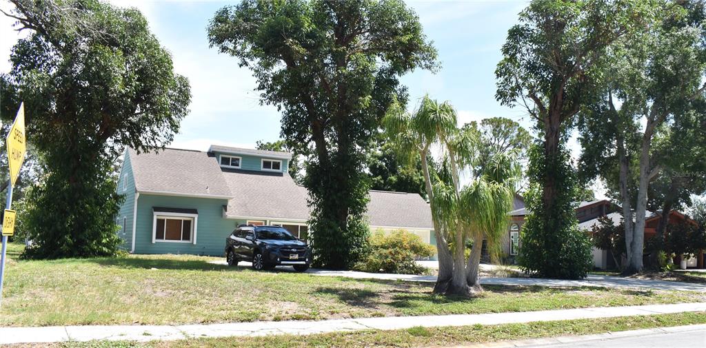 A two-story teal house with a gray roof sits behind a large tree-filled front yard — 7606 15TH AVENUE NW, BRADENTON, FL