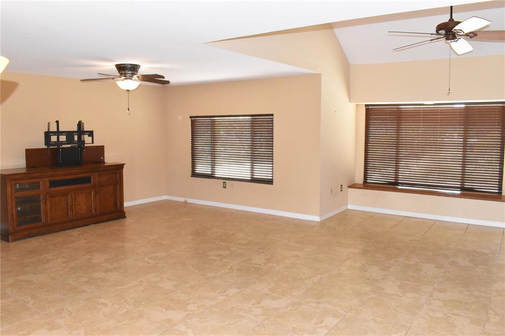 A living room with tan tile flooring, two ceiling fans, and two windows with blinds — 7606 15TH AVENUE NW, BRADENTON, FL