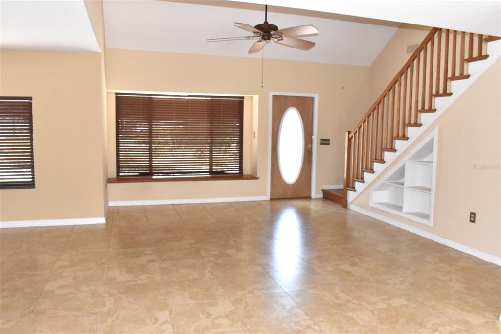 A living room features tan tile flooring, a vaulted ceiling, a staircase, and a front door — 7606 15TH AVENUE NW, BRADENTON, FL