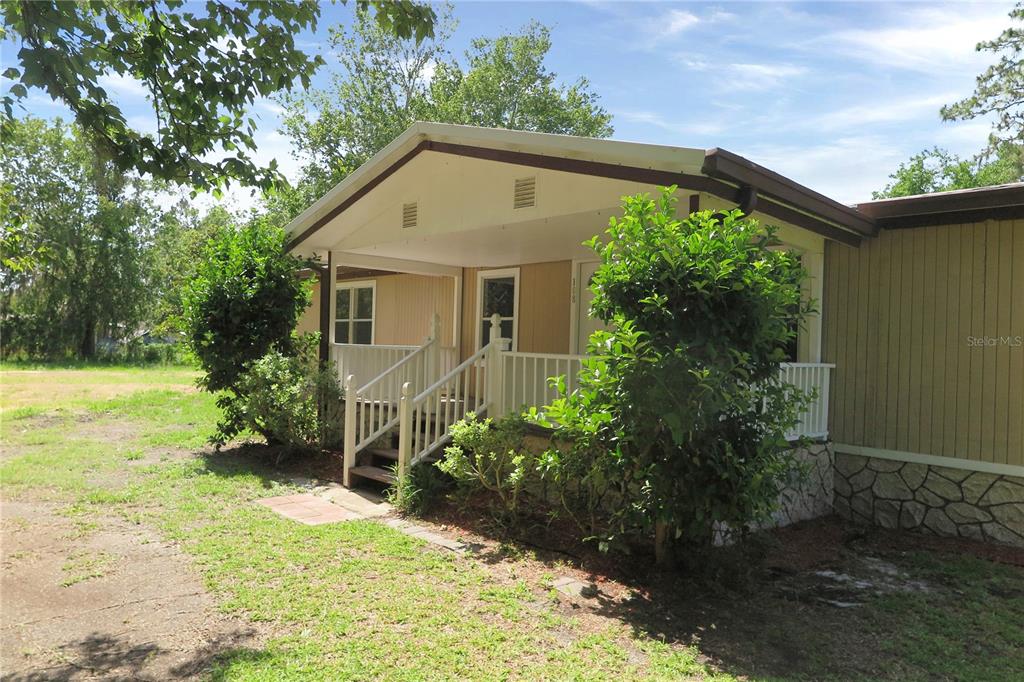 A mobile home exterior features a covered front porch with white railings and stairs — 108 PINESHORE DRIVE, SATSUMA, FL