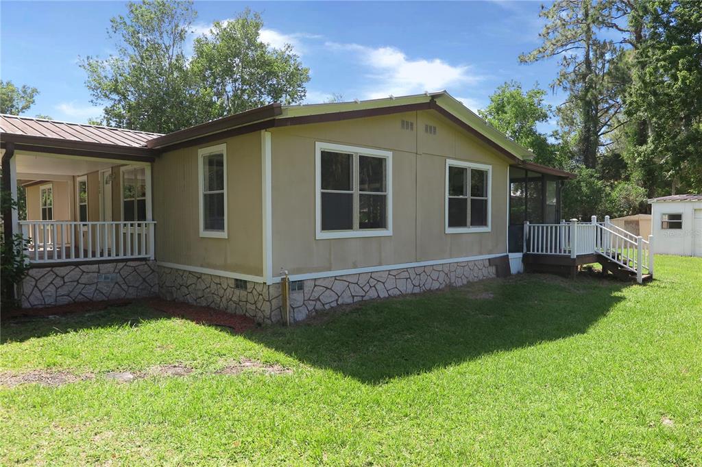 A tan manufactured home with a stone-patterned foundation, a covered porch, and a screened-in area — 108 PINESHORE DRIVE, SATSUMA, FL