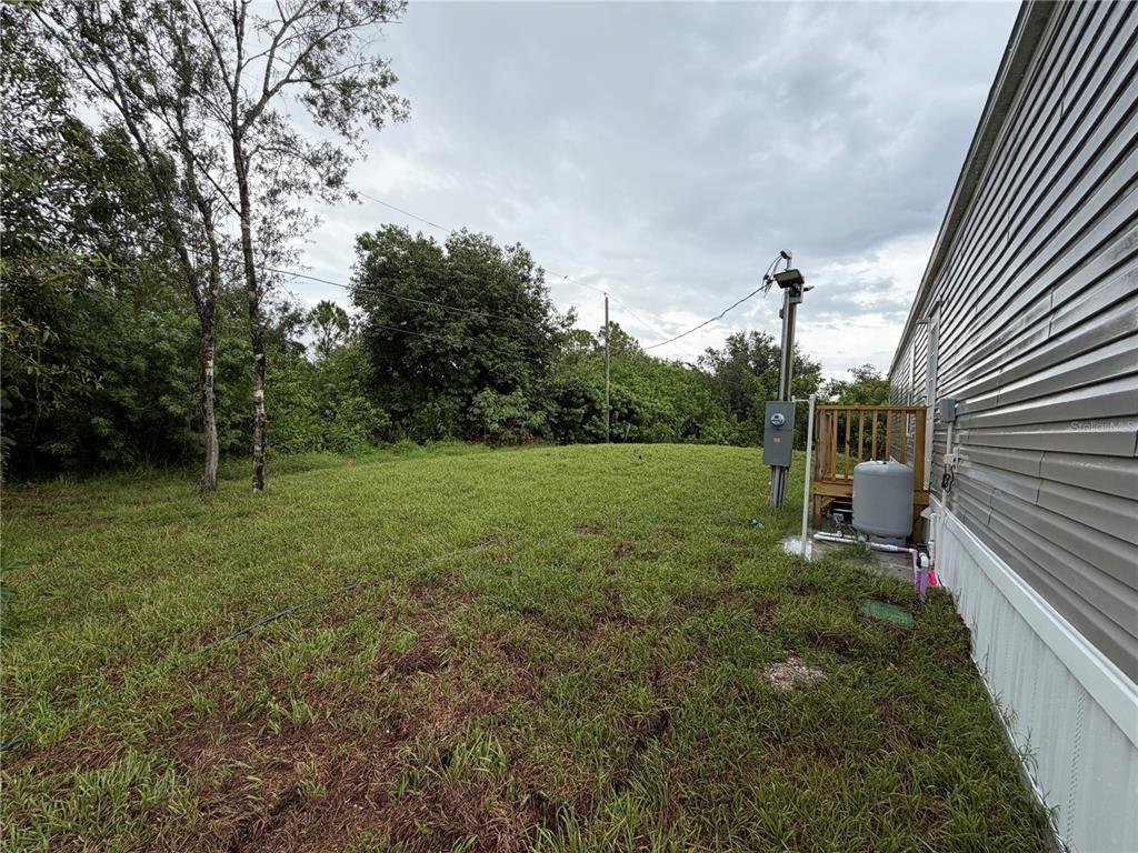A grassy yard sits beside the side wall of a manufactured home with utility equipment — 15492 MANGO DRIVE, PUNTA GORDA, FL