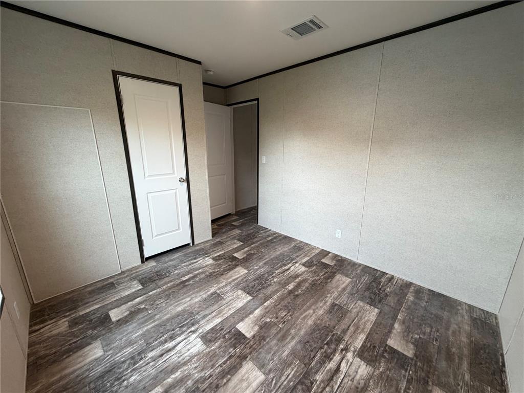An empty room features light-colored paneled walls, dark wood-look flooring, and two white doors — 15492 MANGO DRIVE, PUNTA GORDA, FL
