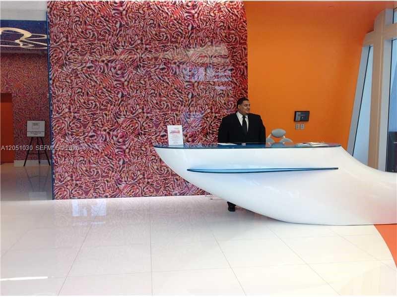 A man in a suit sits behind a modern white reception desk in a lobby — MIAMI, FL