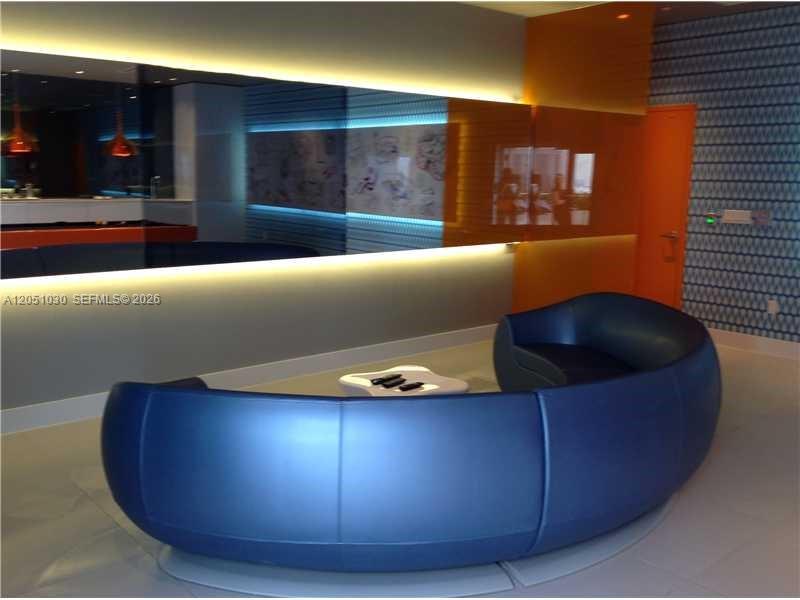 A curved blue sofa sits in a modern room with a large mirror and orange accents — MIAMI, FL