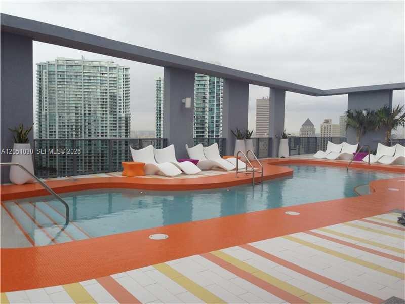 An outdoor rooftop swimming pool features lounge chairs on a bright orange deck — MIAMI, FL