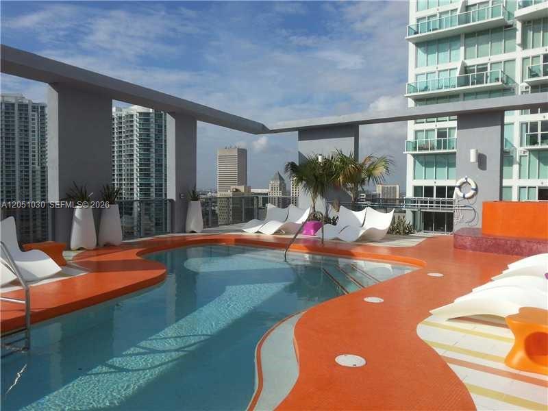 A rooftop swimming pool with orange decking and lounge chairs overlooking a city skyline — MIAMI, FL