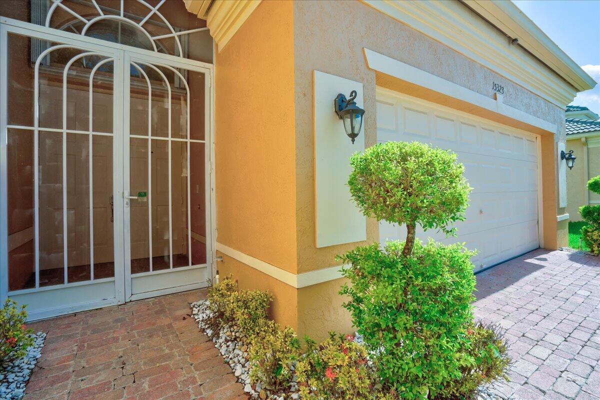 A view of a house exterior featuring a brick walkway, front door, and garage — 15323 Fiorenza Circle, Delray Beach FL 33446, DELRAY BEACH, FL