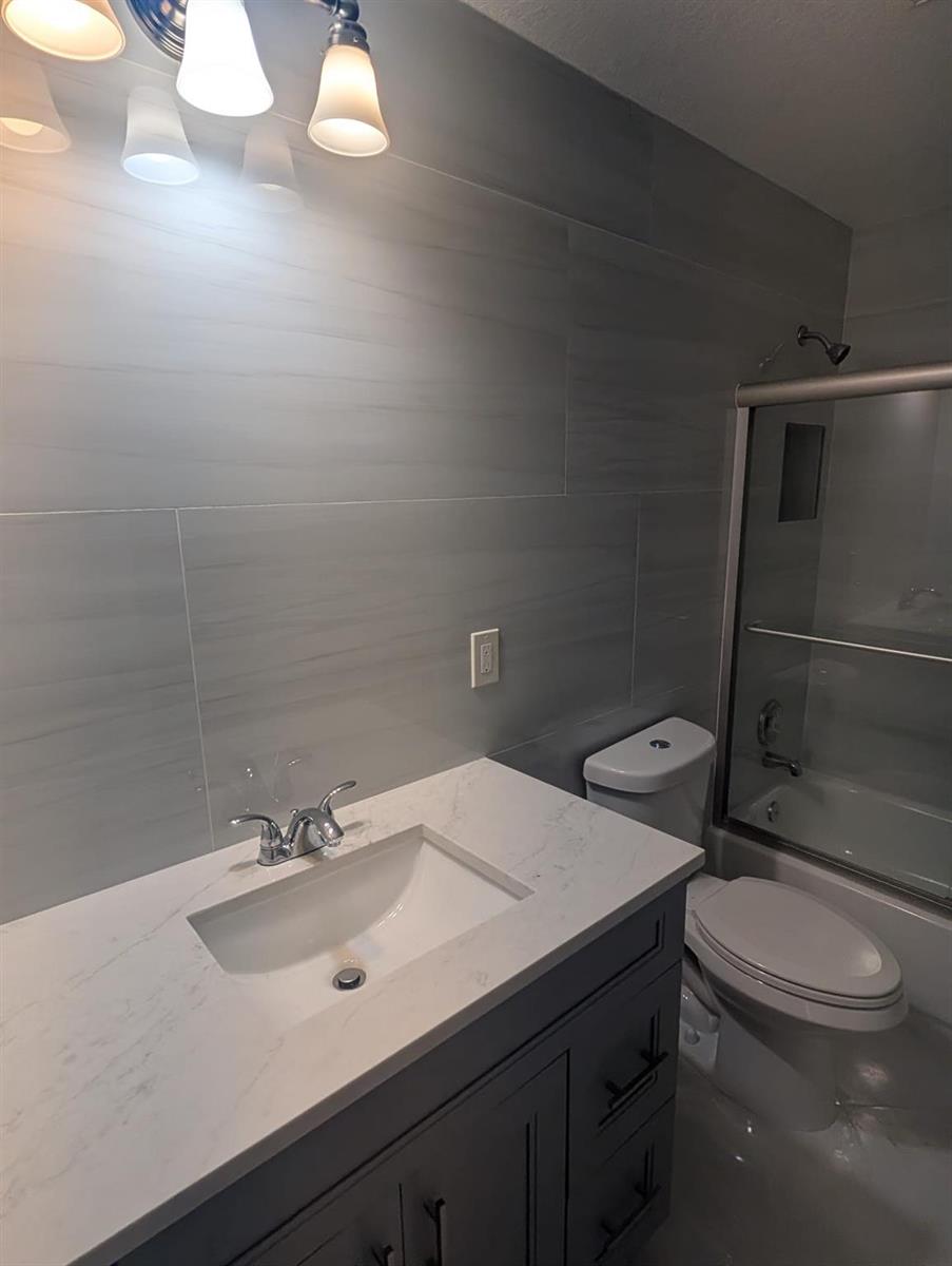 A bathroom featuring a gray vanity, white marble countertop, and gray horizontal wall tiles — 7713 Kimberly Boulevard, North Lauderdale FL 33068, NORTH LAUDERDALE, FL