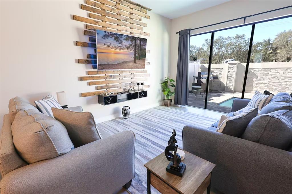 A living room features a wood-slat accent wall, a wall-mounted television, and sliding glass doors — 216 VILLA DOMANI CIRCLE, DAVENPORT, FL