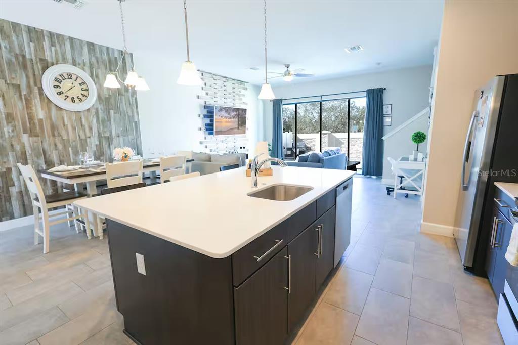 A modern kitchen island with a sink sits before a dining area and living room — 216 VILLA DOMANI CIRCLE, DAVENPORT, FL