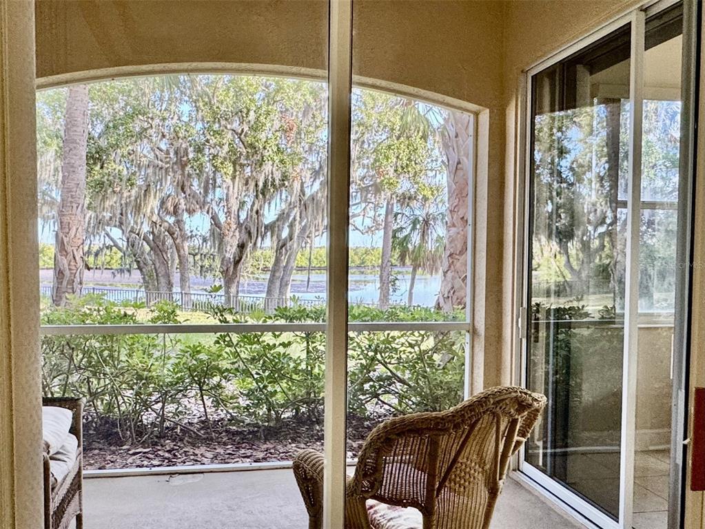A screened-in patio features wicker furniture and a view of trees and a lake — 9411 DISCOVERY TERRACE UNIT 102B, BRADENTON, FL