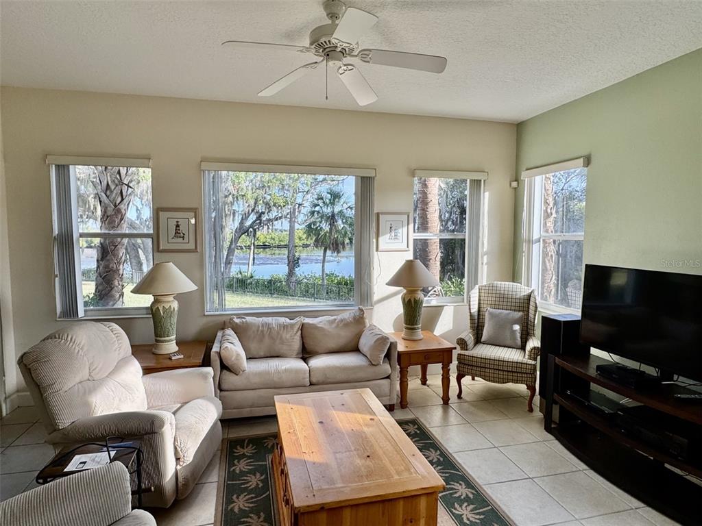 A living room features a ceiling fan, tiled floors, and windows overlooking a waterfront view — 9411 DISCOVERY TERRACE UNIT 102B, BRADENTON, FL