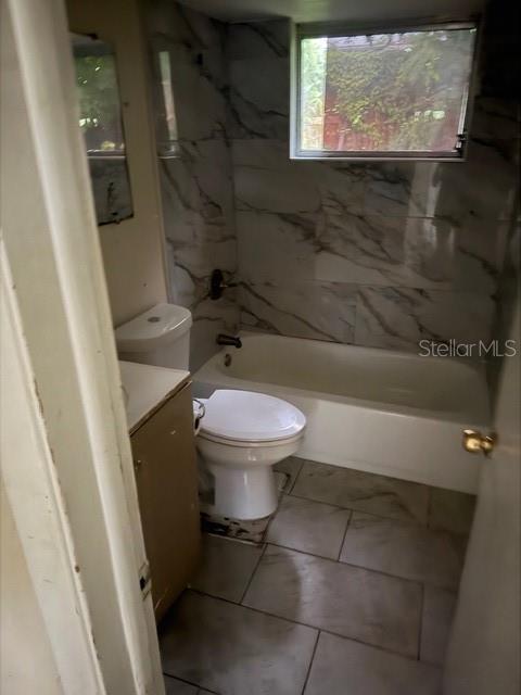 A bathroom features a white toilet, a bathtub with marble-patterned tile walls, and tiled flooring — 3331 CLYDESDALE DRIVE, HOLIDAY, FL