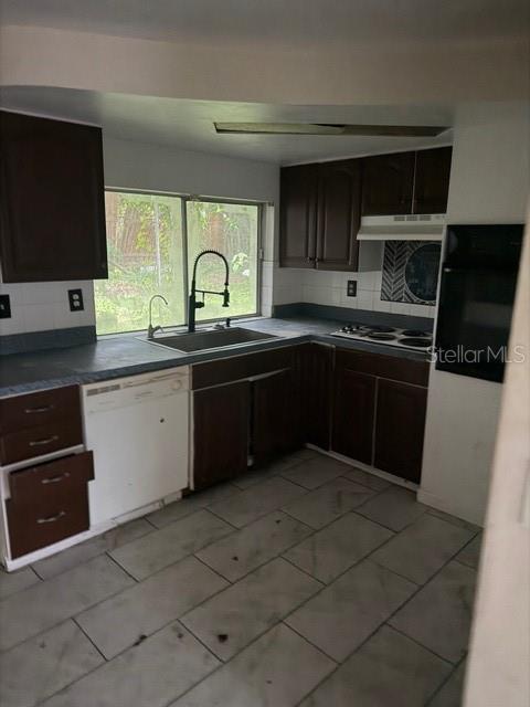 A kitchen features dark wood cabinets, a white dishwasher, a window, and light-colored floor tiles — 3331 CLYDESDALE DRIVE, HOLIDAY, FL