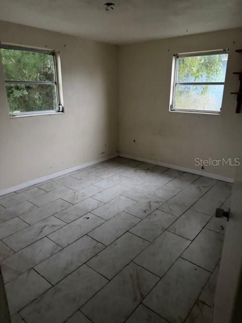 An empty bedroom features light-colored walls, two windows, and white tile flooring — 3331 CLYDESDALE DRIVE, HOLIDAY, FL